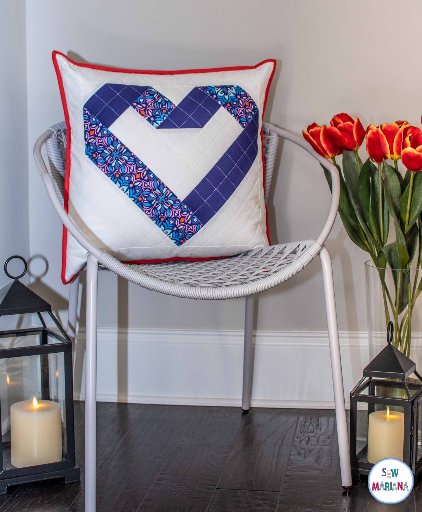 A pillow made with one block of the in my heart quilt pattern it's shown on a light gray chair and candle lights on the floor